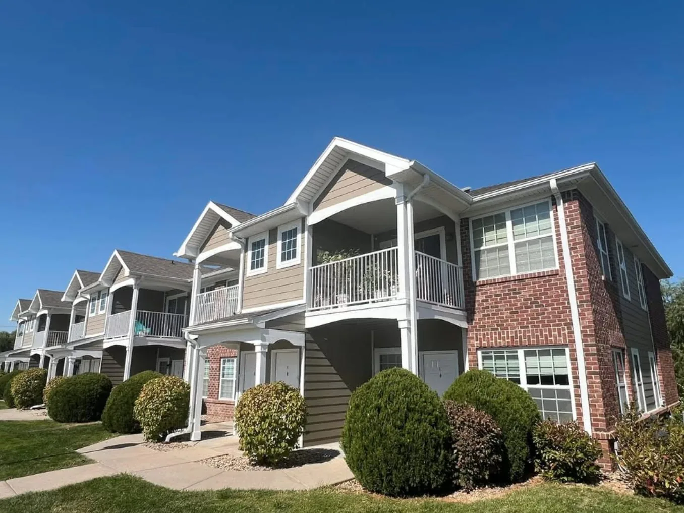 Exterior painting in Lincoln, NE: two story apartment building with red brick, tan lap siding, white trim and white balcony railings