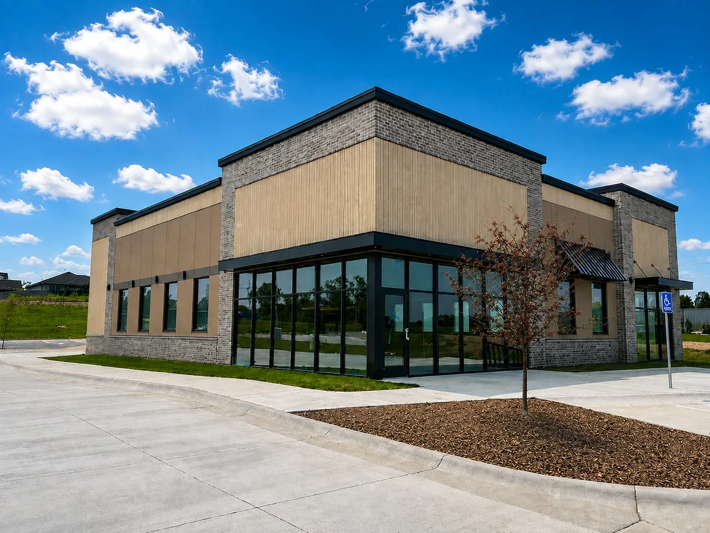 Single story retail building with gray brick, tan exterior panels and black storefront glass, commercial facade work from a stucco repair contractor in Lincoln, NE