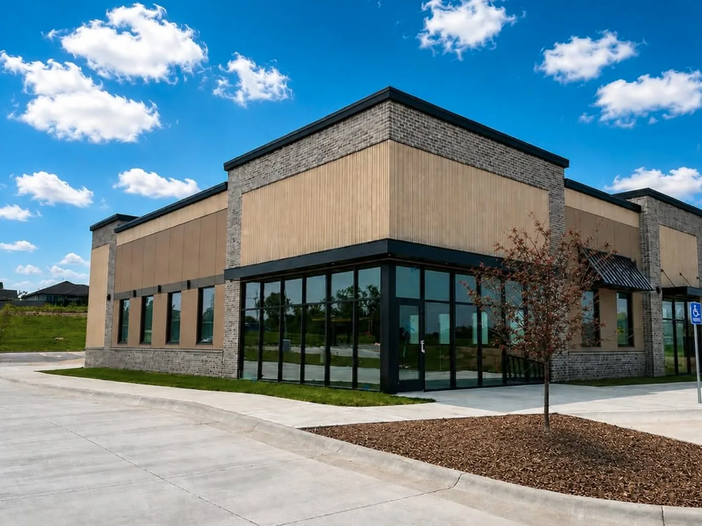 Corner of a retail building with gray brick piers, tan panel facade and black framed storefront windows