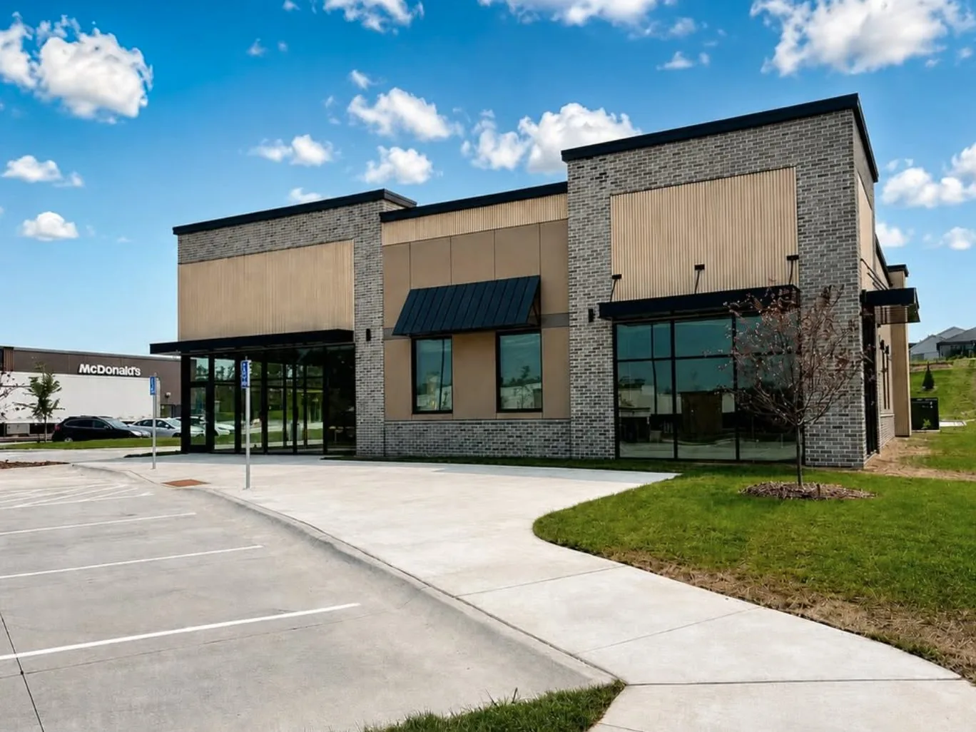 Single story retail building with gray brick piers, tan panel facade, black metal awning and storefront glass, finished by a commercial exterior contractor in Nebraska