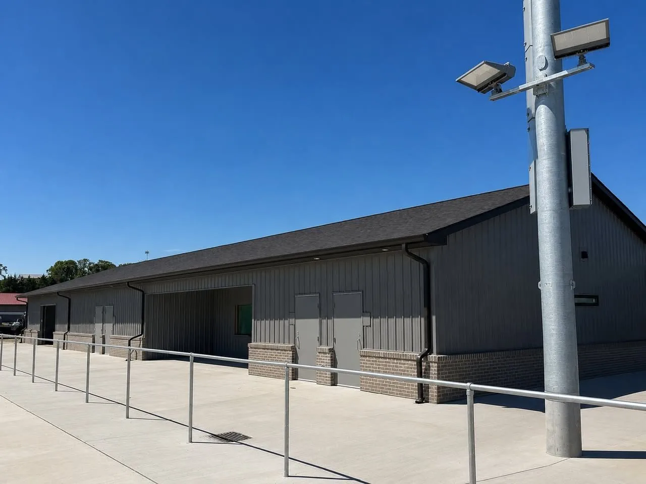 Long gray metal sided building with a brick wainscot and black gutters