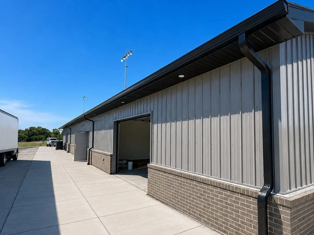 Gray metal building with black gutters and downspouts over a brick base