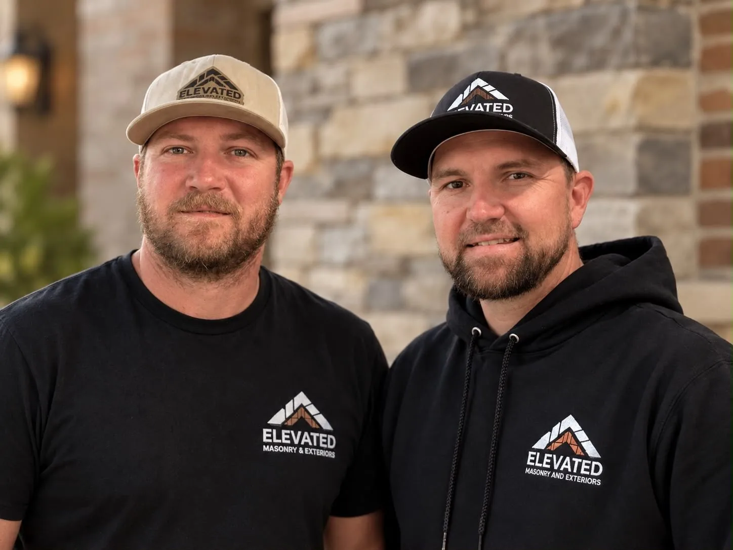 Two members of the Elevated Masonry & Exteriors team in branded caps and shirts