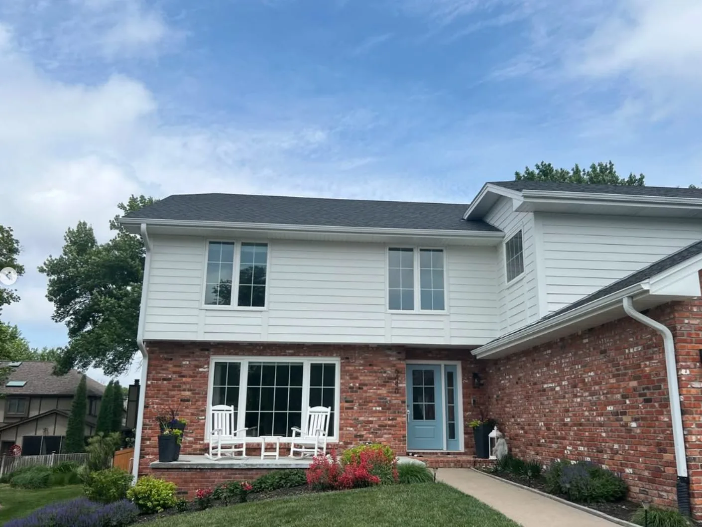 Two story house with a red brick lower level, white lap siding and gutters