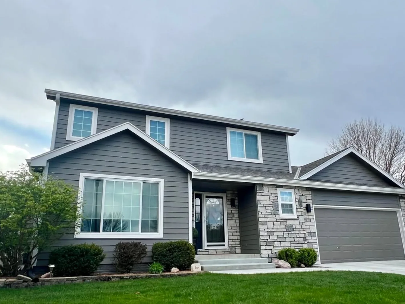 Two story home with gray lap siding, white trim and a stone veneer entry, siding work by Elevated, siding contractors in Lincoln, NE